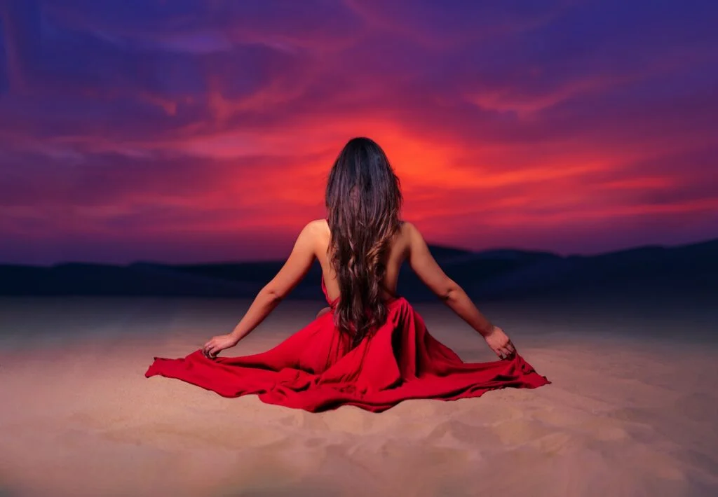 woman in red dress sitting on sand during sunset