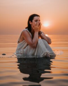 a woman sitting in the water with her hands to her face