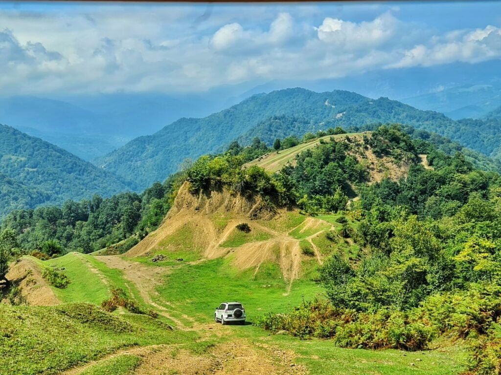 white car on green grass field near green mountains under blue sky during daytime
