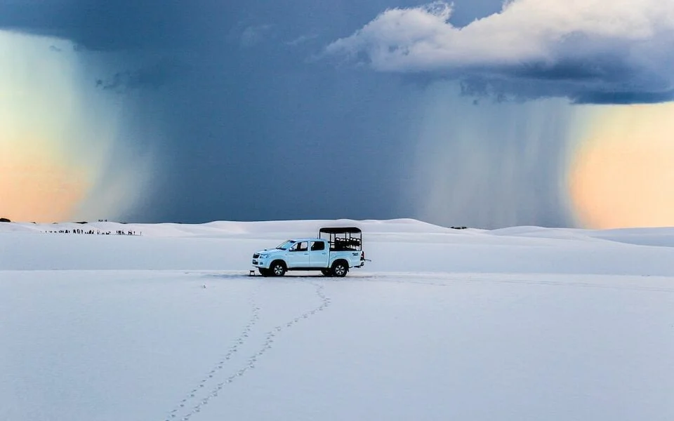 a truck driving across a snow covered field under a cloudy sky