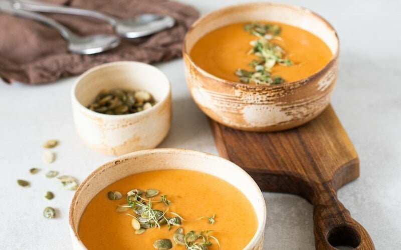 two bowls of carrot soup on a white table