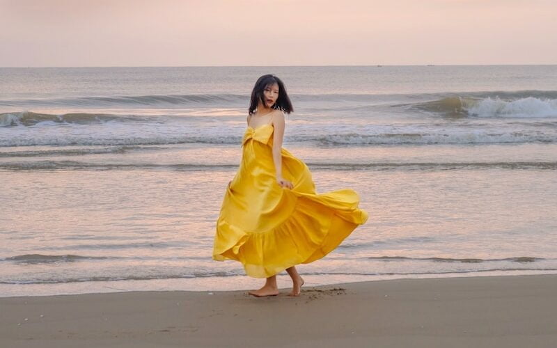 a woman in a yellow dress walking on the beach
