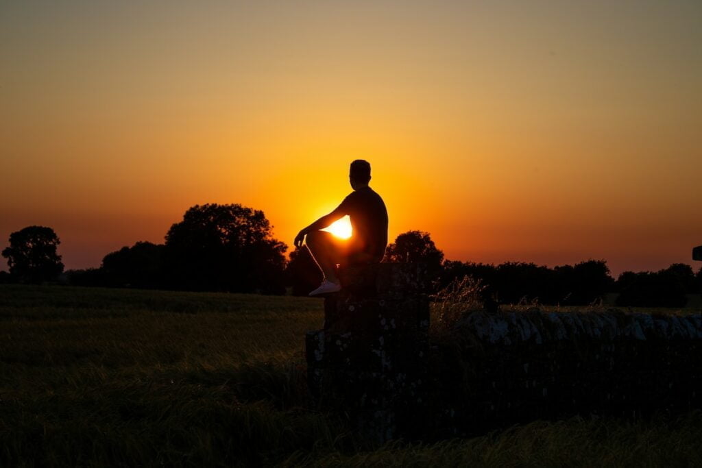 a man standing in a field with the sun setting behind him