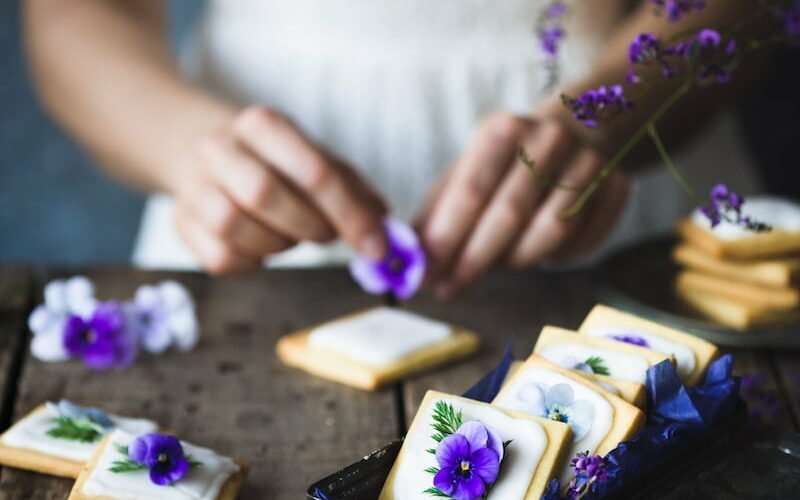 a woman in a white dress is decorating cookies with purple flowers