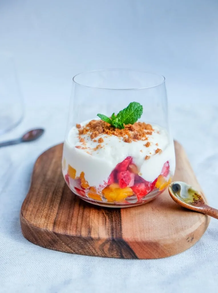 Close-up of a fruit and yogurt parfait with mint garnish on a wooden board, perfect for dessert lovers.