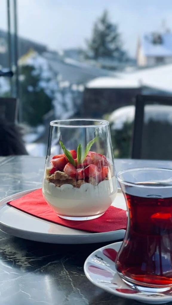 Elegant yogurt parfait with strawberries and a glass of tea in a snowy outdoor setting.