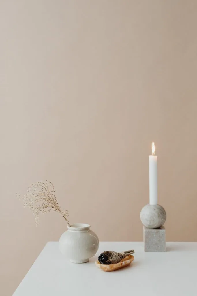 Peaceful minimalist setting with candle, sage, and vase on table.