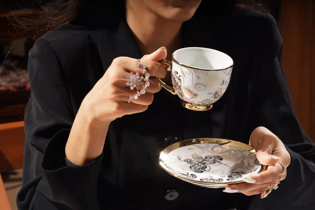 A close-up of a woman in black attire holding a beautifully decorated teacup with matching saucer.