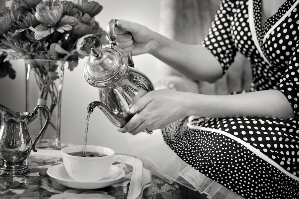 Elegant vintage tea setting with woman pouring tea from silver teapot.