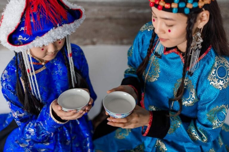 Mother and daughter in Mongolian attire sharing a cultural drink ceremony.