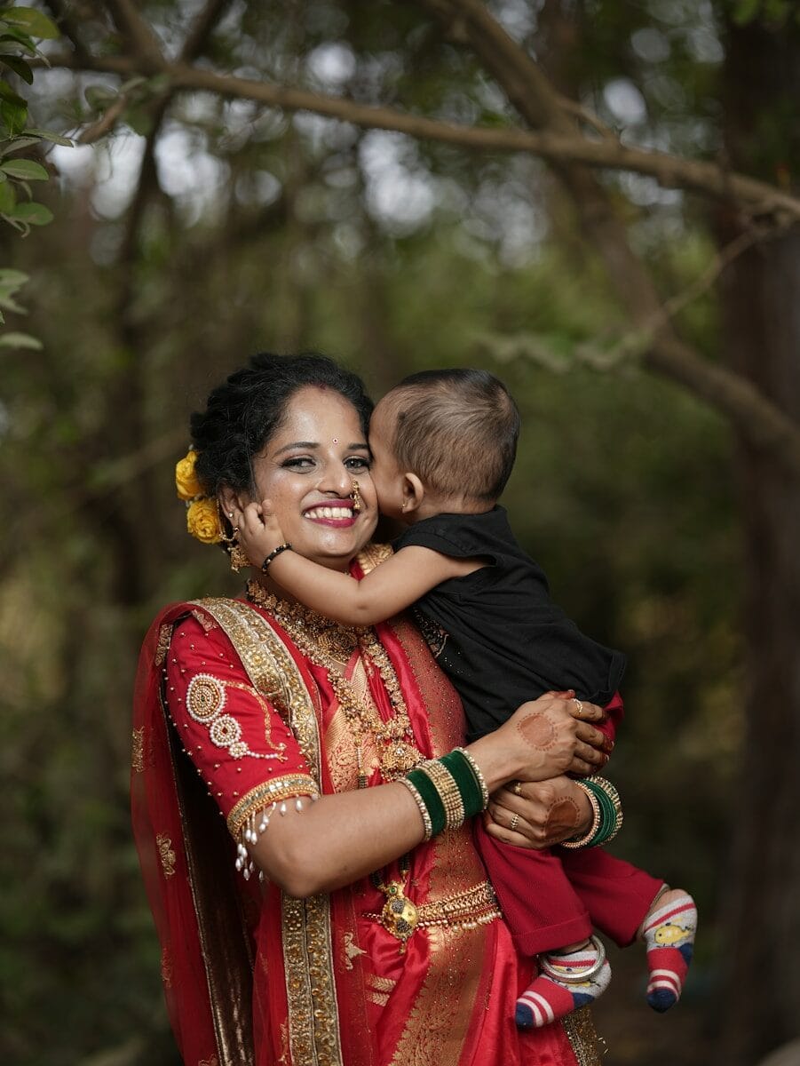 A woman in a red and gold sari holding a baby