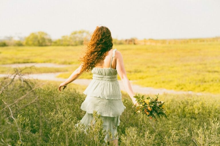 A woman walks away through a grassy field.