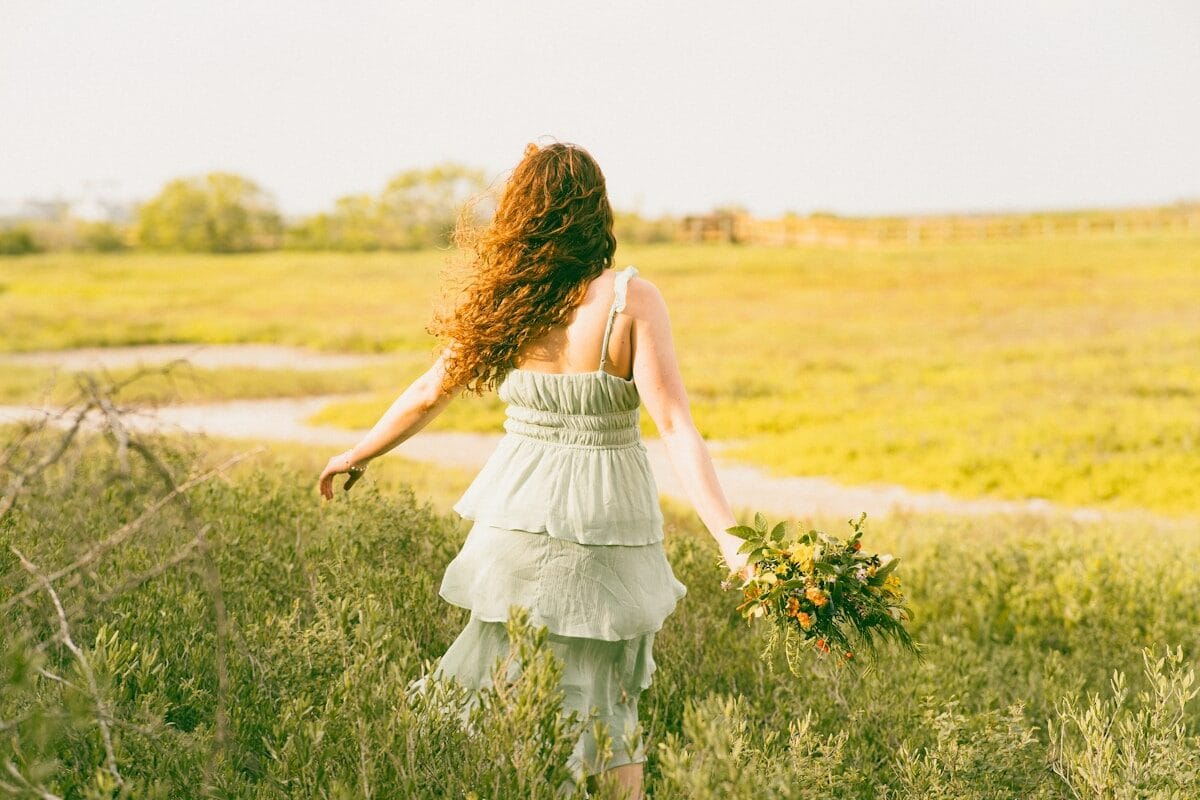 A woman walks away through a grassy field.